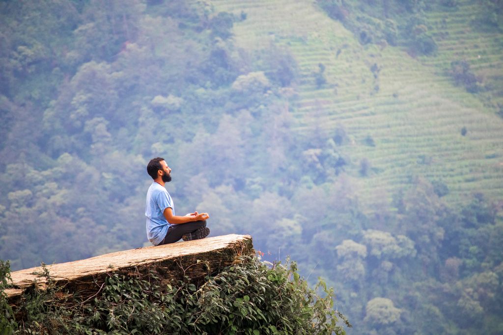 Man meditating on a cliff with lush green mountains in Ghandruk, Nepal.